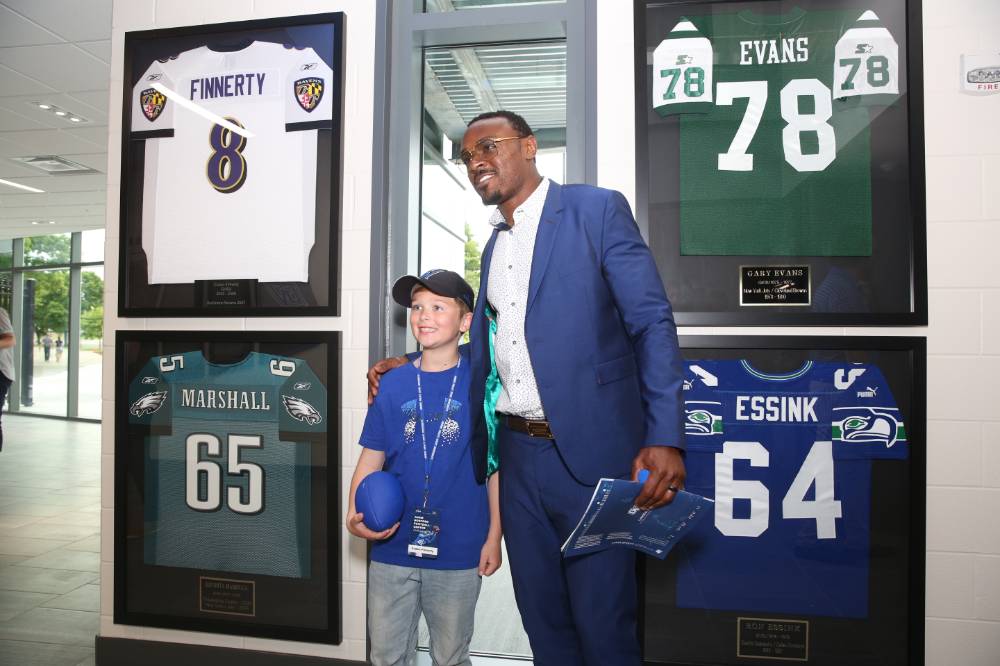 Guest posing with a child in front of four framed jerseys at the Jamie Hosford Football Center dedication.